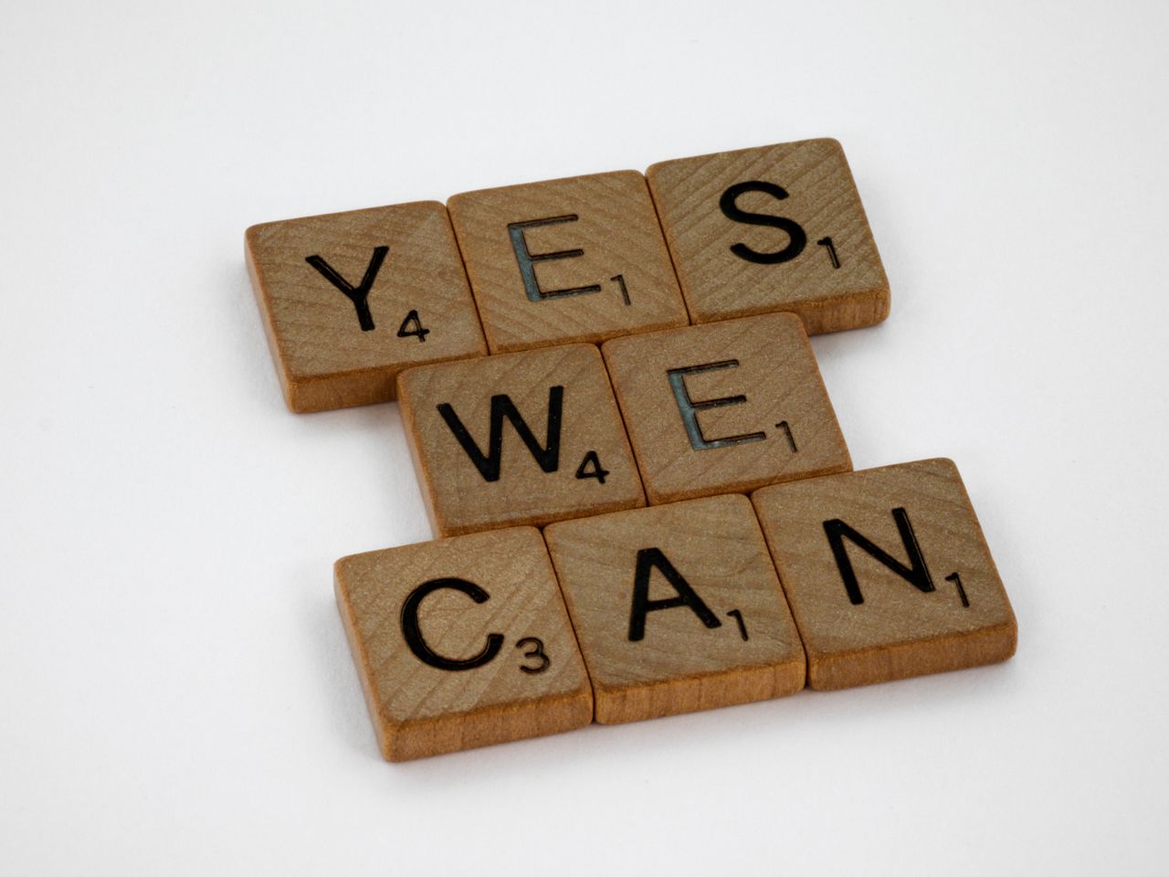 Wooden Scrabble tiles arranged to spell 'Yes We Can', emphasizing motivation on a white backdrop.